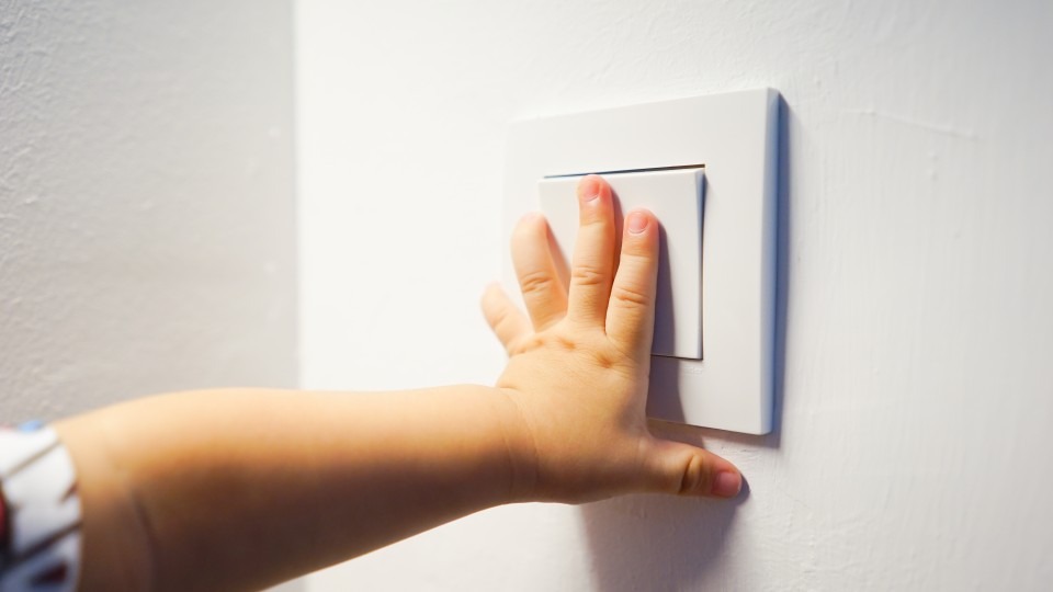 Das Bild zeigt eine Kinderhand, die einen Lichtschalter bedient. 