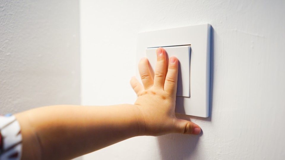 Das Bild zeigt eine Kinderhand, die einen Lichtschalter bedient.