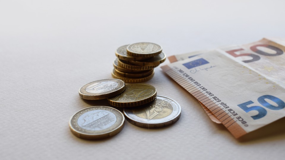 In der Mitte sind Euro-Münzen gestappelt und rechts daneben liegen zwei 50 Euro Scheine
