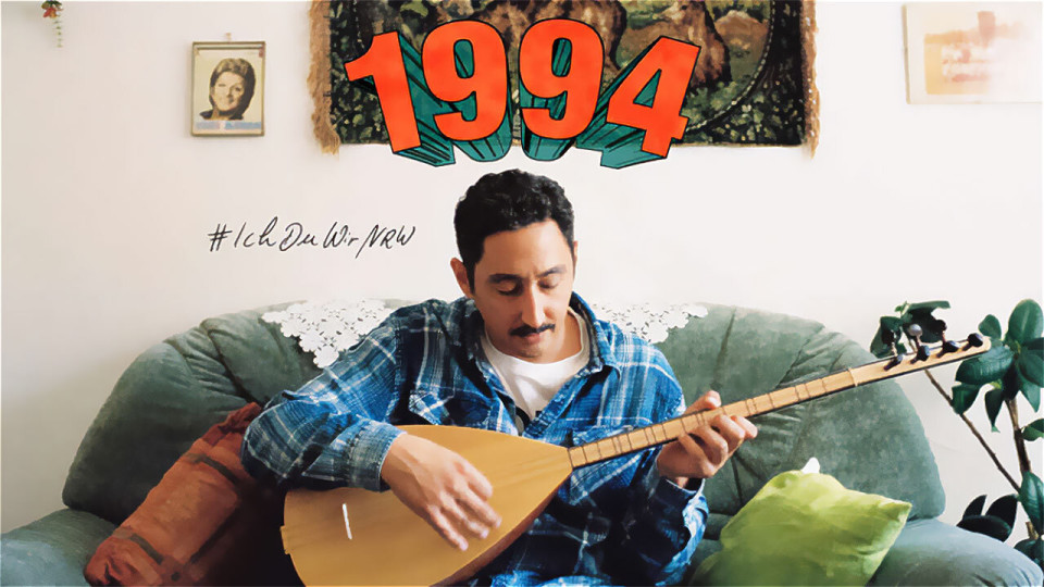 Mann spielt Saz auf Sofa, Jahr 1994, Hashtag: #IchDuWirNRW.