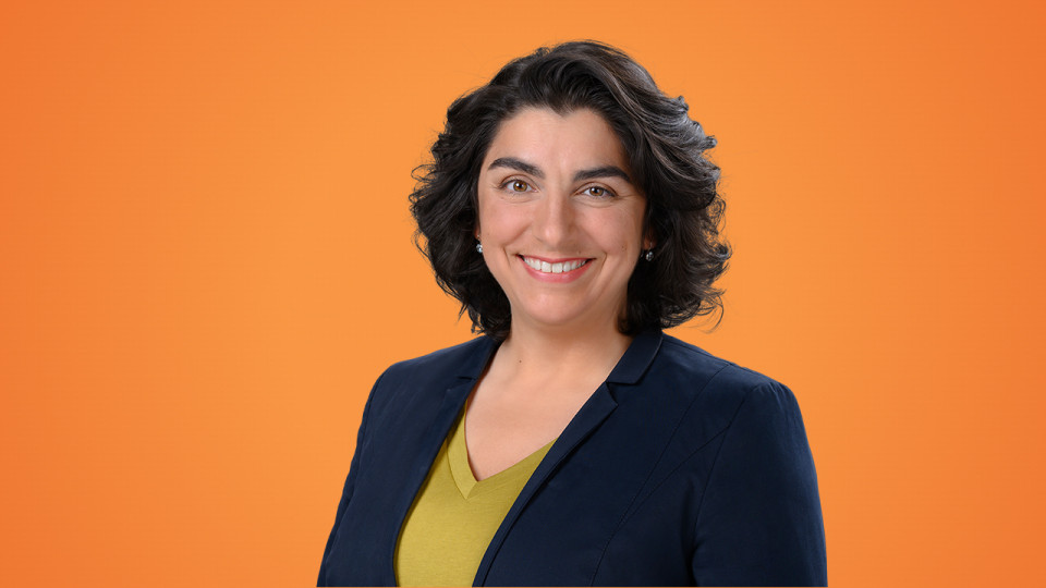 Person lächelt freundlich vor einem orangefarbenen Hintergrund.