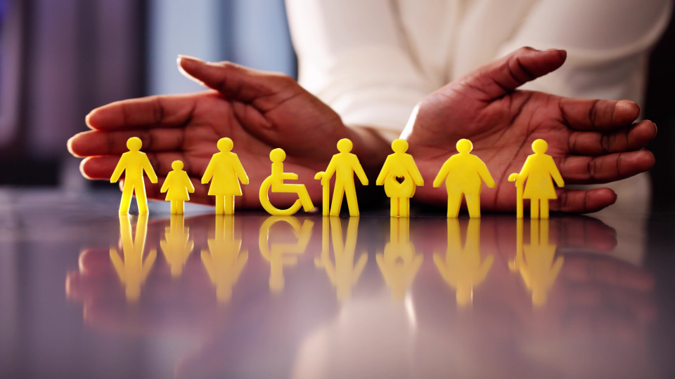 Zwei schützende Hände umgeben eine Reihe gelber Figuren, die Menschen unterschiedlicher Altersgruppen und Bedürfnisse darstellen, darunter Kinder, Erwachsene, ältere Personen und eine Person im Rollstuhl