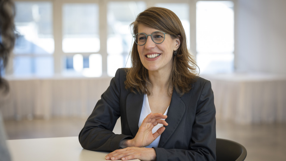 Minsiterin Verena Schäffer sitzt lächelnd an einem Tisch in einem Besprechungsraum