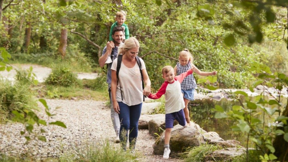 Mutter, Vater und drei Kinder laufen zusammen durch einen Wald.