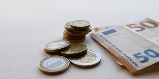 In der Mitte sind Euro-Münzen gestappelt und rechts daneben liegen zwei 50 Euro Scheine