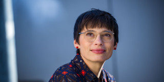 Ministerin Paul schaut nachdenklich lächelnd nach oben links. Der Oberkörper ist nur abgeschnitten zu sehen. 