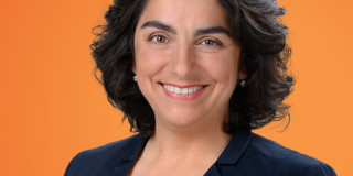 Eine Frau lächelt freundlich vor einem orangefarbenen Hintergrund.