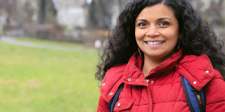 Frau in roter Jacke lächelt draußen vor Felsen im Hintergrund.