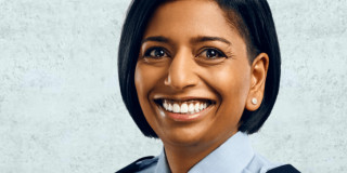 Lächelnde Polizistin in Uniform vor hellem Hintergrund.