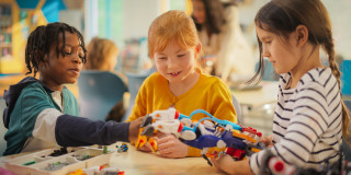 Drei Kinder bauen gemeinsam einen bunten Roboterarm in einem Klassenraum