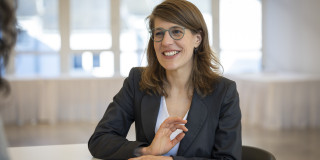 Minsiterin Verena Schäffer sitzt lächelnd an einem Tisch in einem Besprechungsraum
