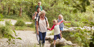 Mutter, Vater und drei Kinder laufen zusammen durch einen Wald.