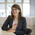 Minsiterin Verena Schäffer sitzt lächelnd an einem Tisch in einem Besprechungsraum